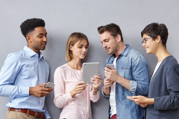 Candid shot of talented creative young men and women business partners having discussion on startup project, developing successful strategy and business plan, using gadgets. Teamwork and cooperation